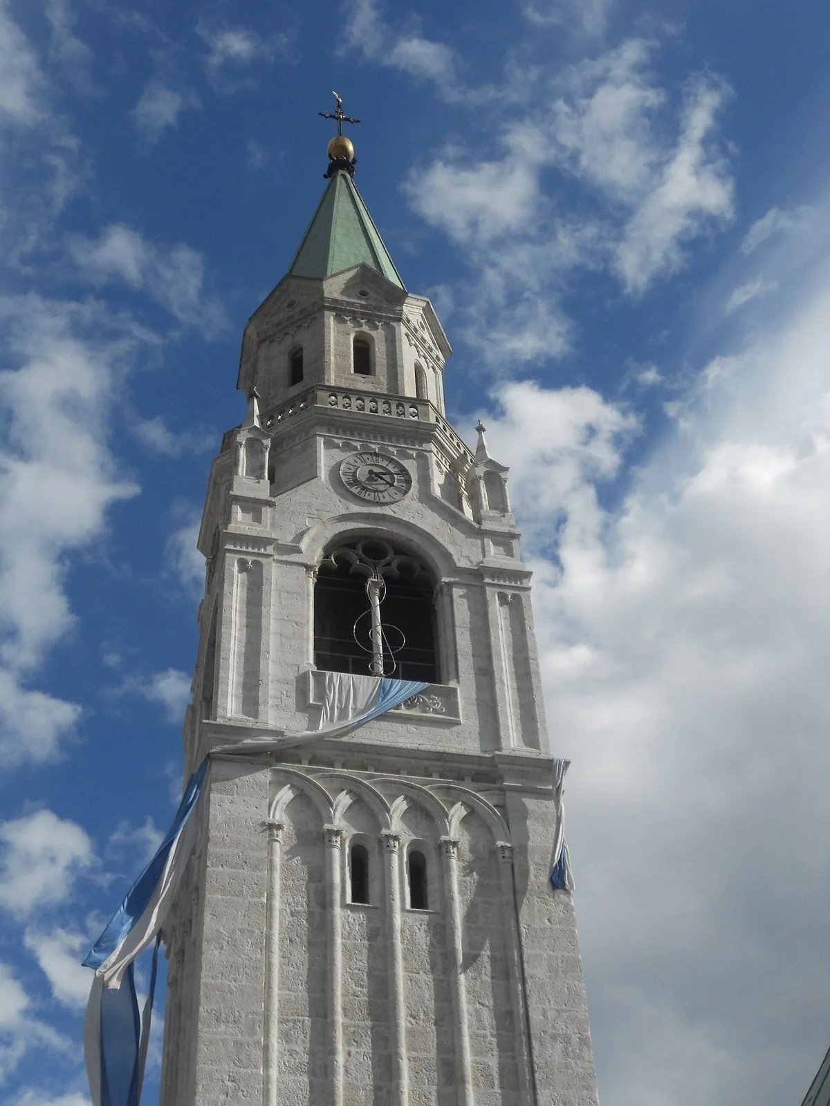 Il campanile in pietra chiara della Basilica dei Santi Filippo e Giacomo a Cortina d'Ampezzo contro un cielo azzurro